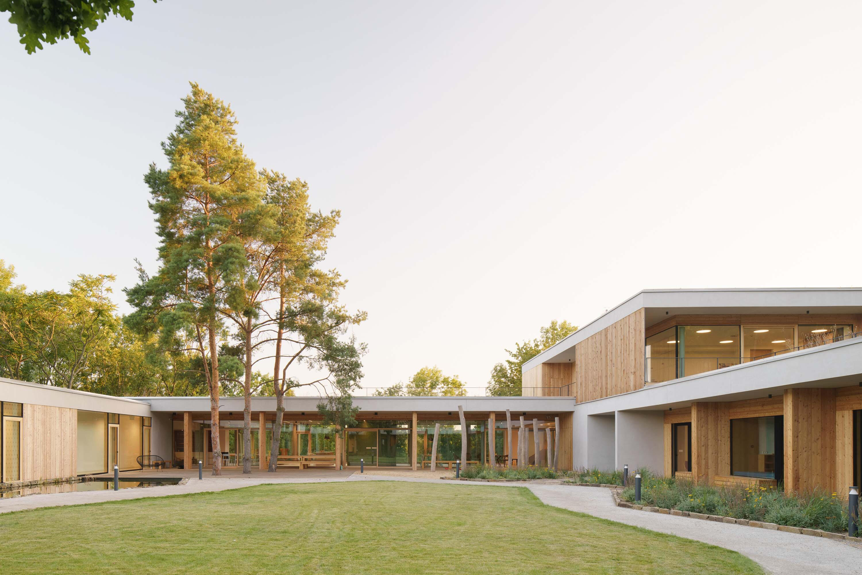 House for Juliet: a low timber and white building around a lawn courtyard with tall pines.