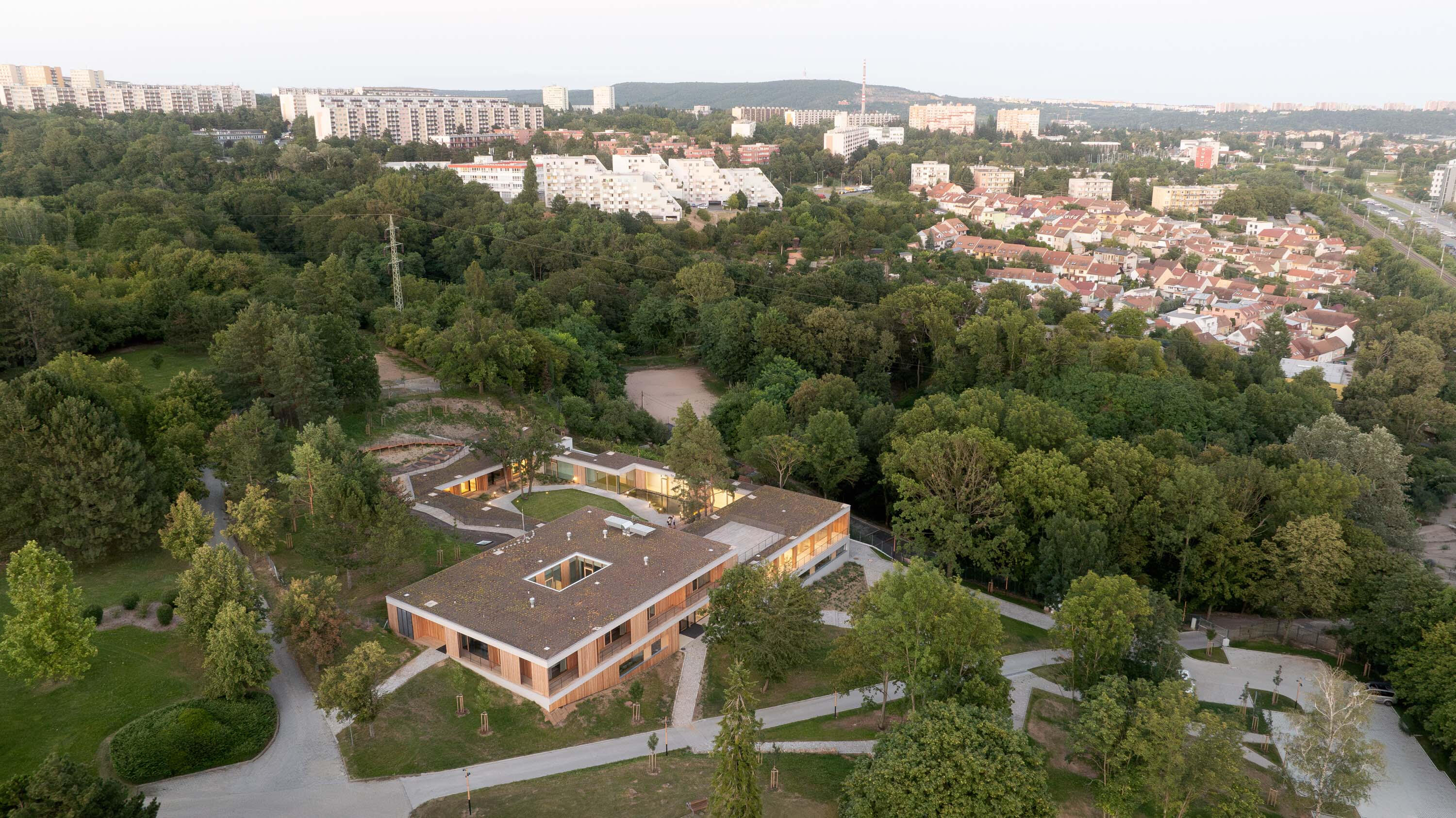 Aerial view of the hospice among mature trees, with Brno's housing estates behind.